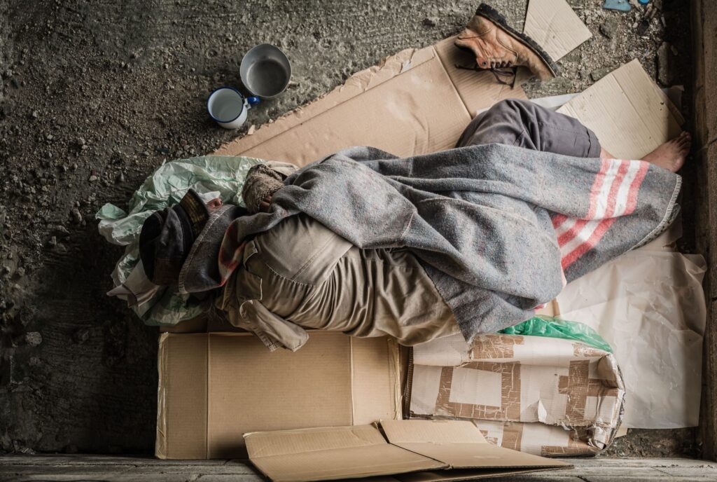 A homeless man using cardboard boxes for a makeshift bed.