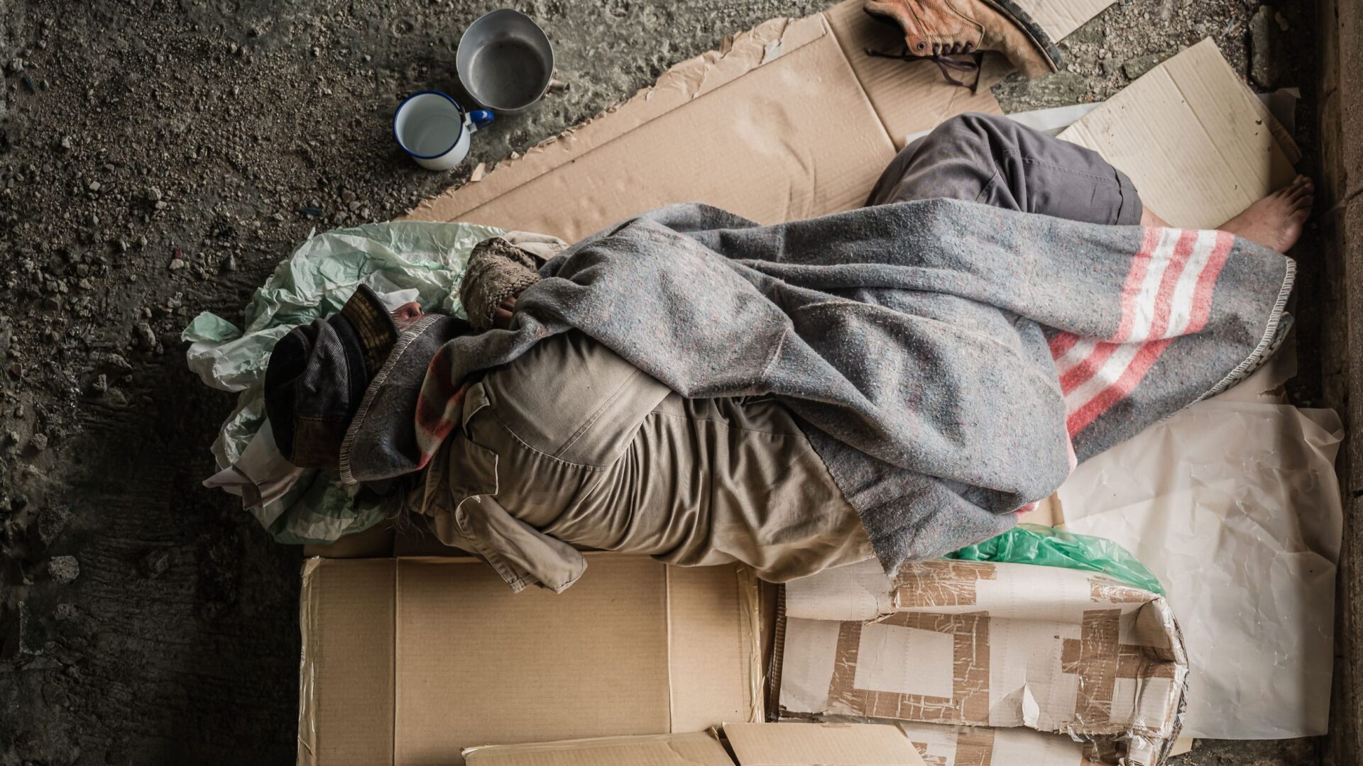 A homeless man using cardboard boxes for a makeshift bed.